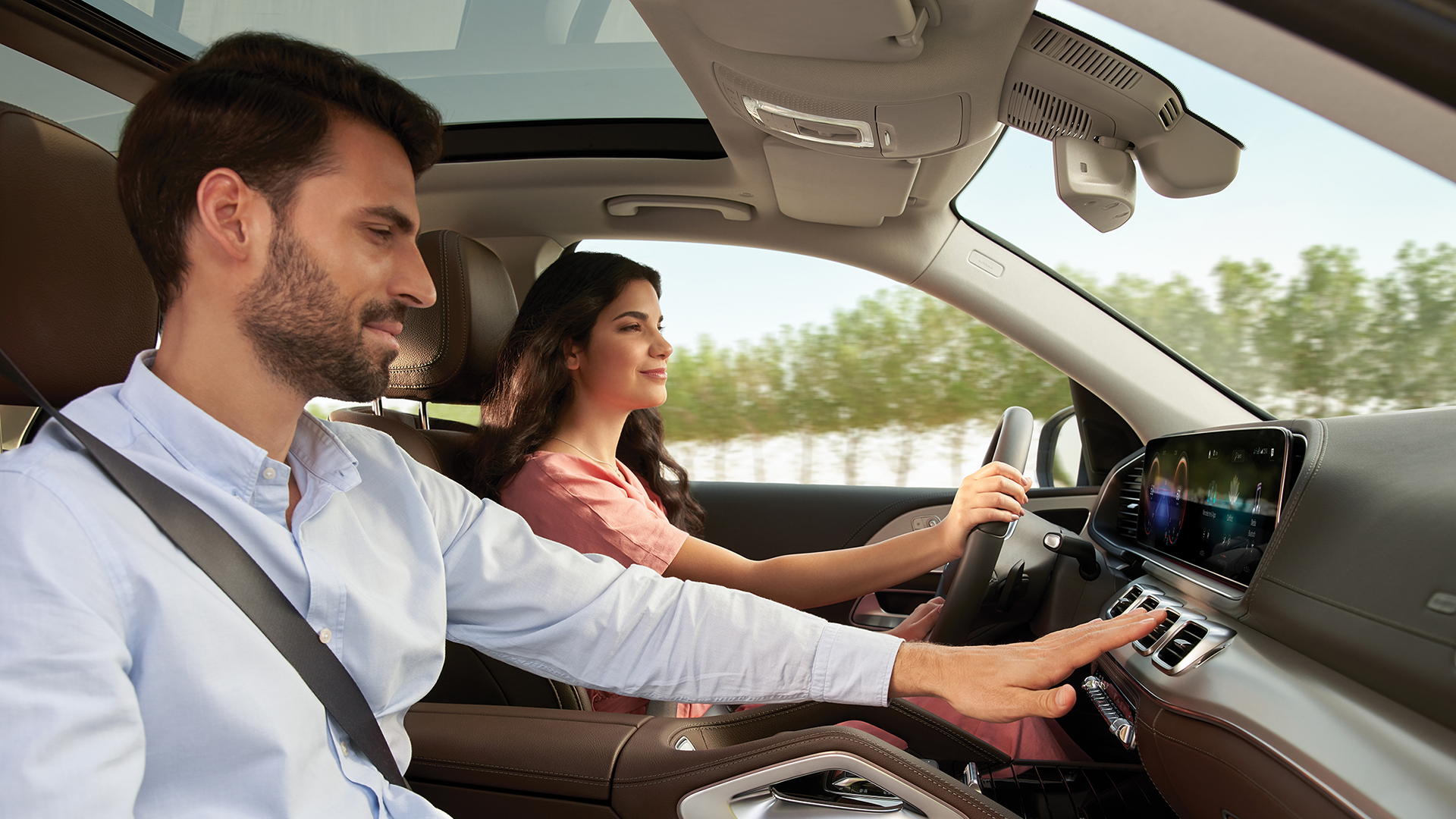 Mies ja nainen autossa. Toinen koettaa kädellään ilmaa tuuletusaukkojen edessä.