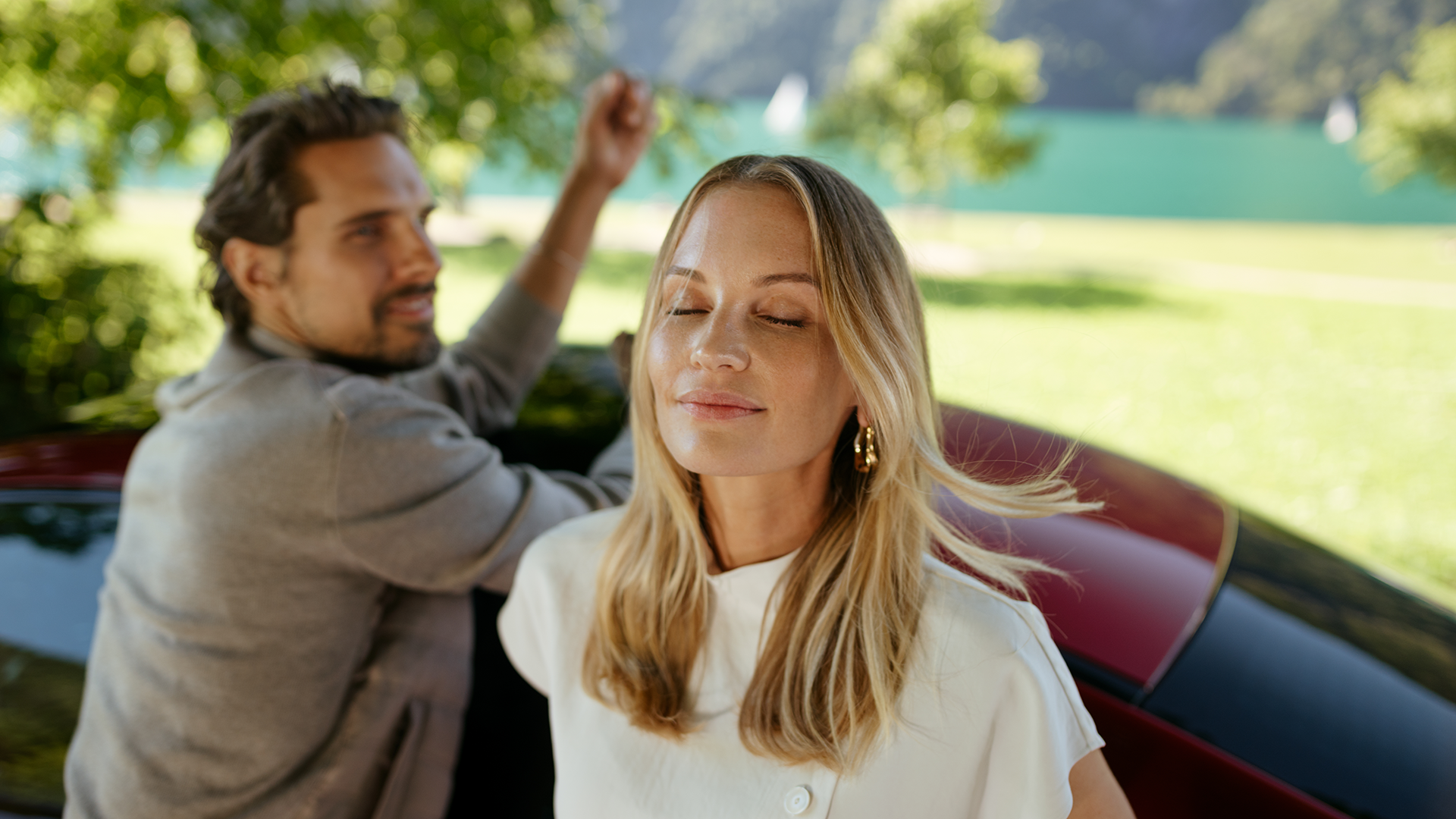 Pariskunta punaisen Mercedes-Benz-auton vieressä rannalla.