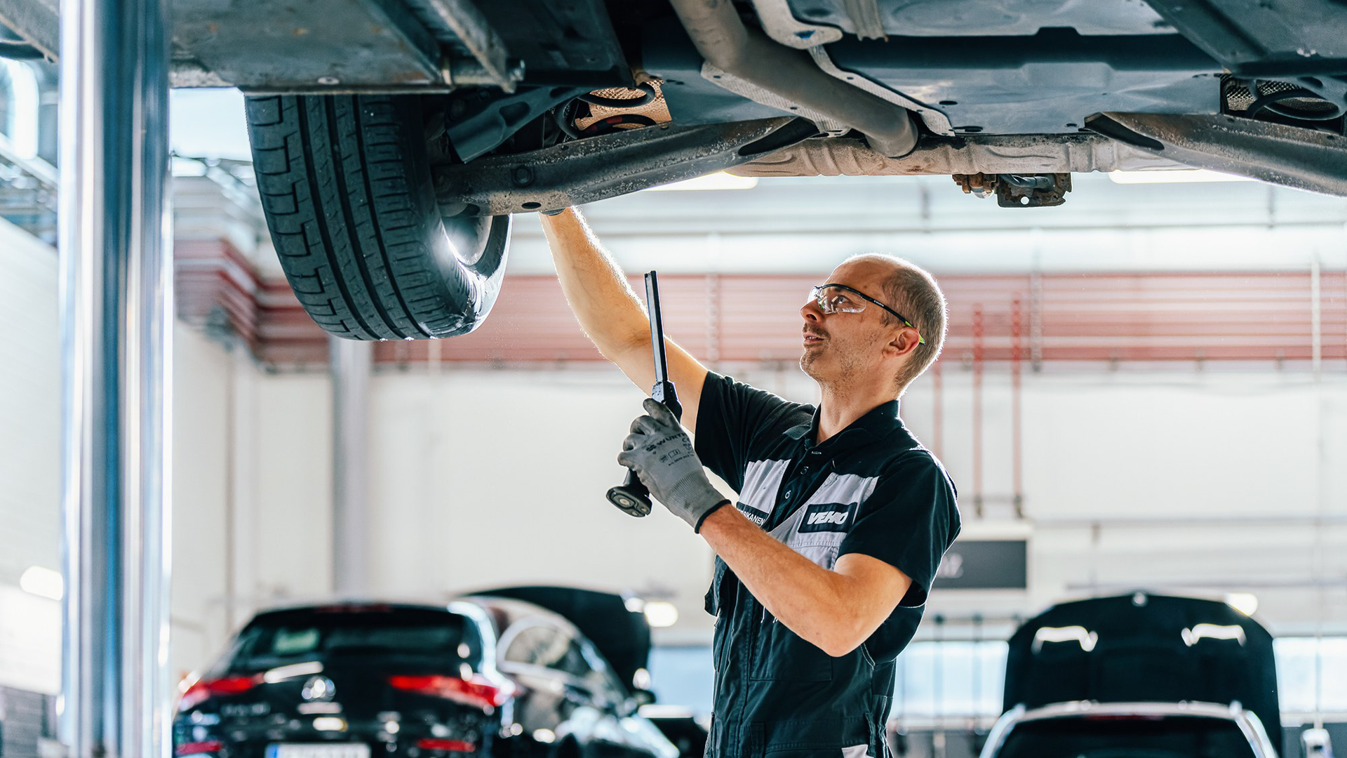 Mercedes-mekaanikko auton alla tarkistaa tukivarsien välyksiä.