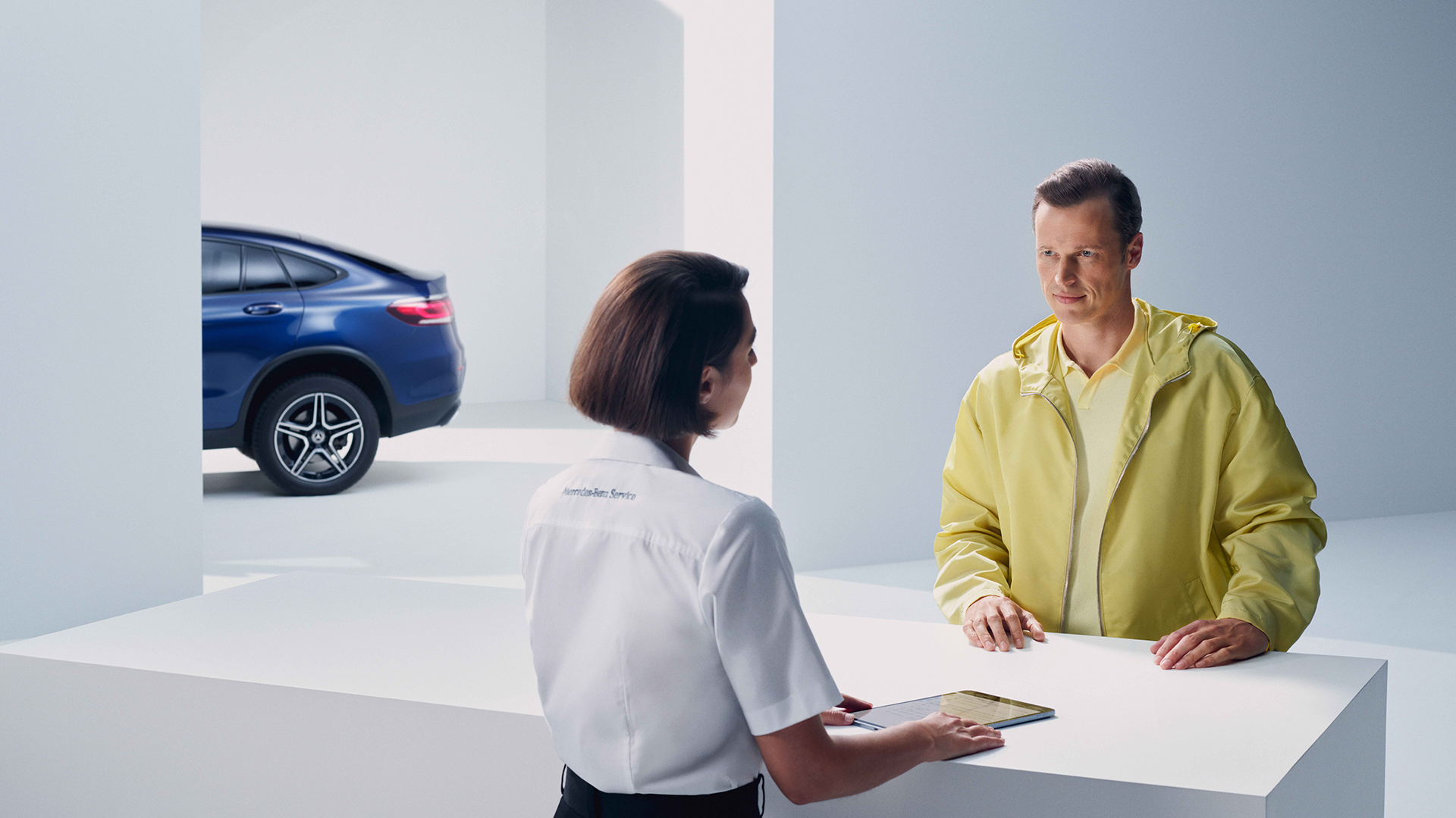 Asiakaspalvelutilanne, jossa taustalla kulman takaa näkyy sinisen Mercedes-maasturin takaosa.