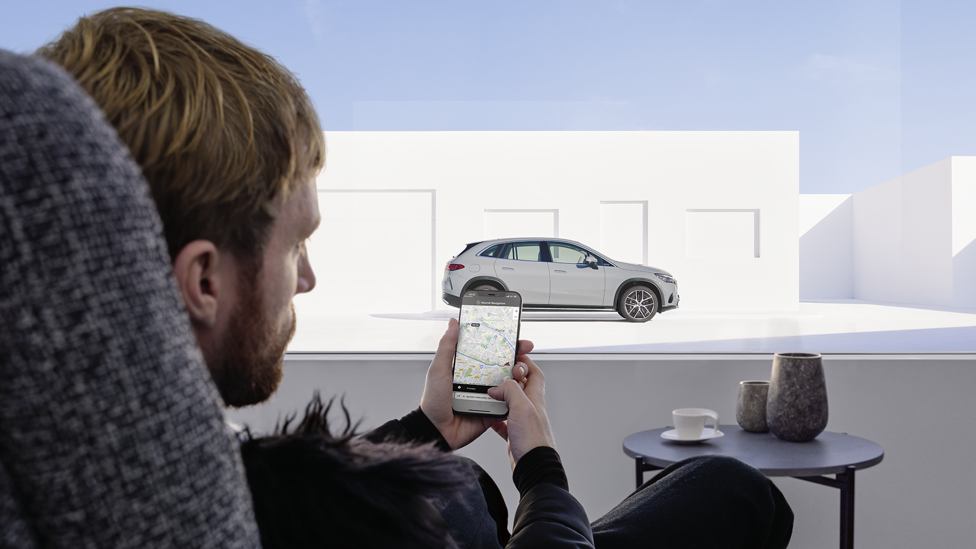 Mies puhelin kädessä, suunnittelee ajoreittiä. Taustalla Mercedes-täyssähköauto.