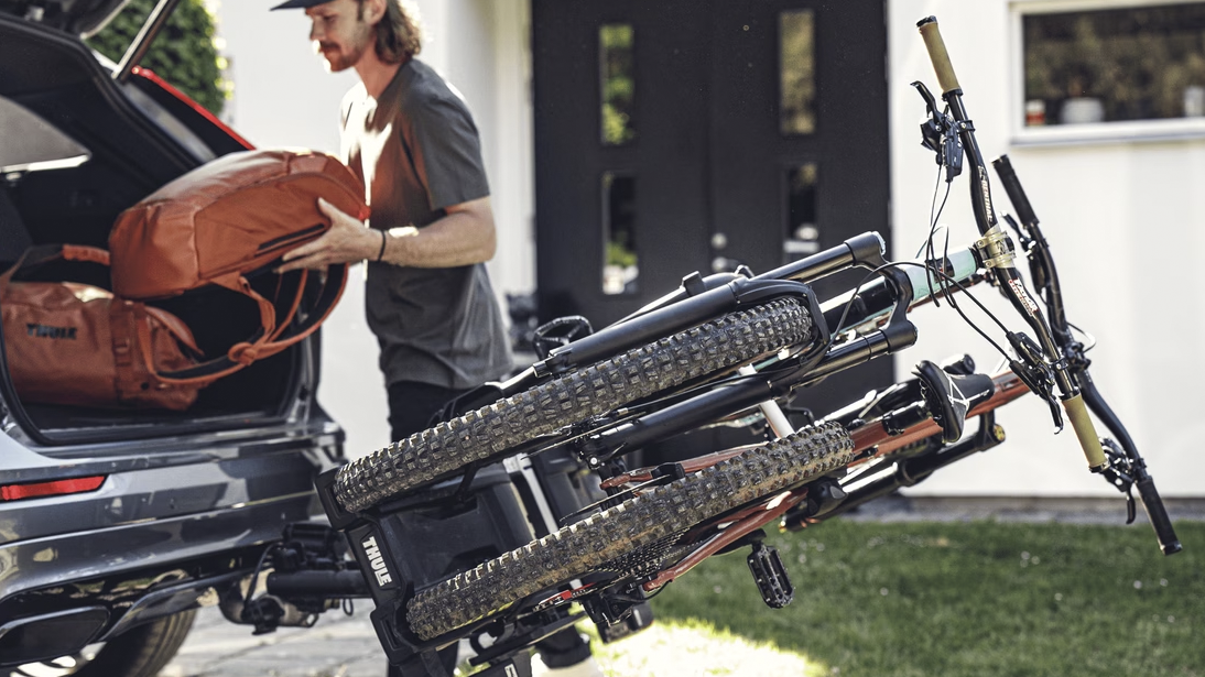 Mies pakkamassa auton takakontin kasseja. Vetokoukussa kaksi polkupyörää Thulen taittuvassa pyörätelineessä.