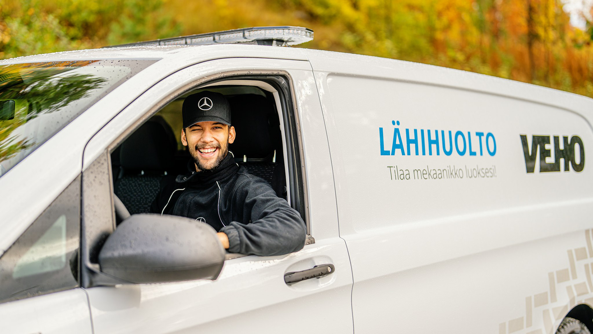 Vehon mekaanikko Lähihuoltoautossa, katsoo kameraan ja hymyilee.