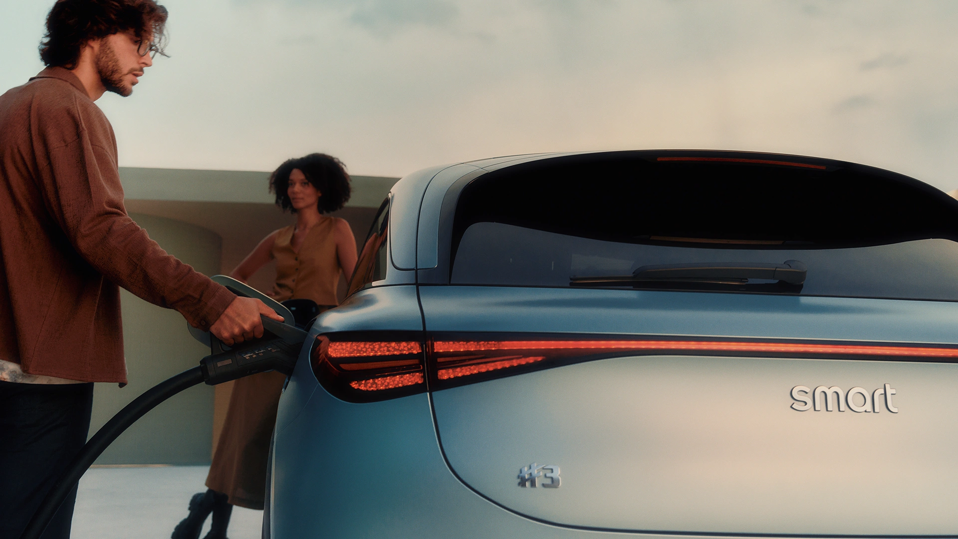 Mies lataamassa smart #3 autoa, naisen katsellessa auton edessä.