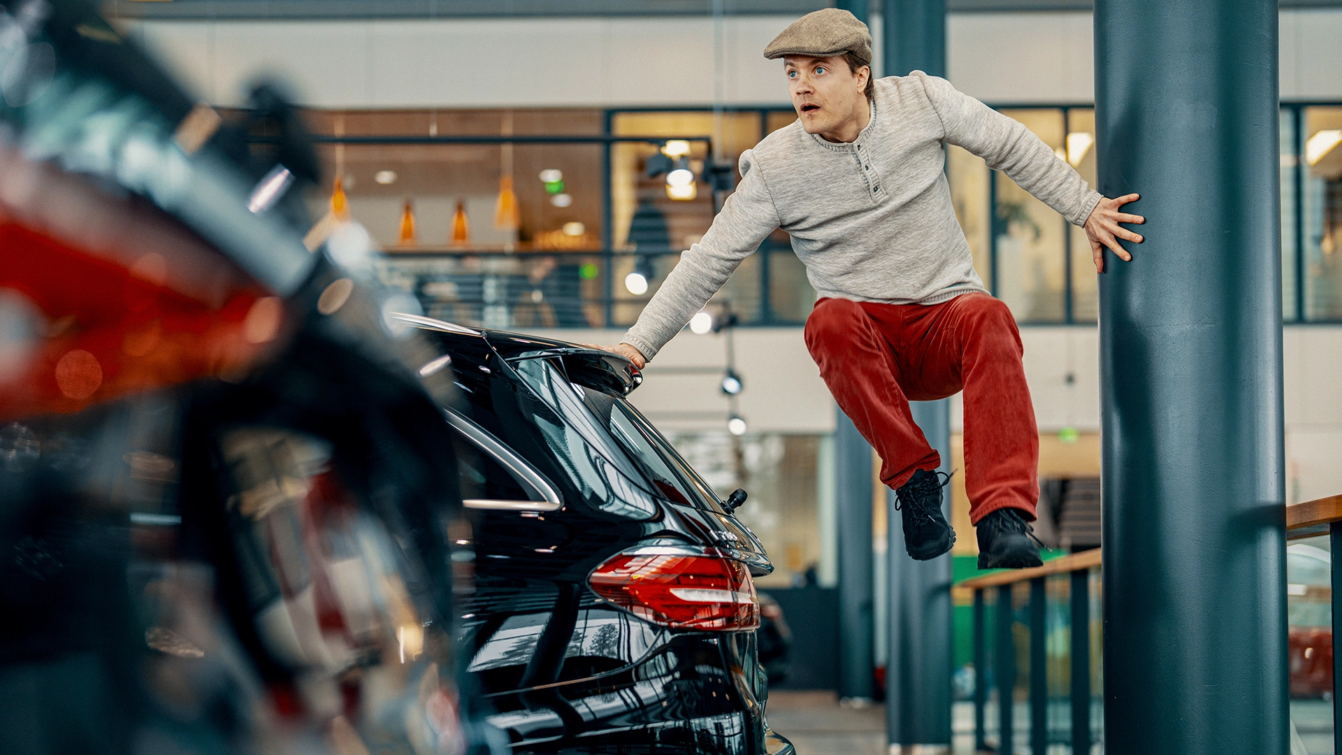 Mies hyppää ja on ilmassa auton takana autoliikkeessä.